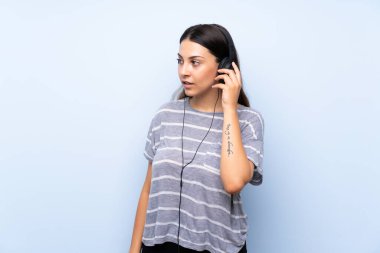Izole mavi arka plan üzerinde genç esmer kadın kulaklık ile müzik dinlerken