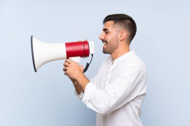 Izole mavi arka plan üzerinde sakallı yakışıklı adam bir megafon ile bağırıyor