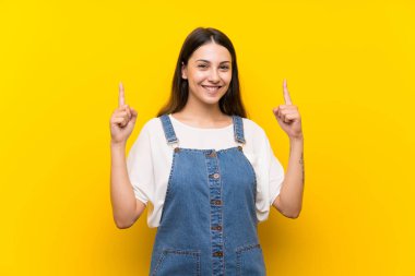 İzole edilmiş sarı arka planda kot giyen genç bir kadın harika bir fikre işaret ediyor.