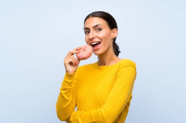 İzole mavi arka plan üzerinde bir donut tutan genç kadın