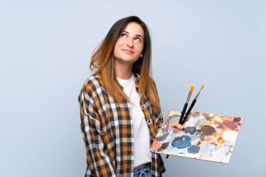 Genç ressam kadın izole edilmiş mavi arka planda gülümserken yukarı bakıyor