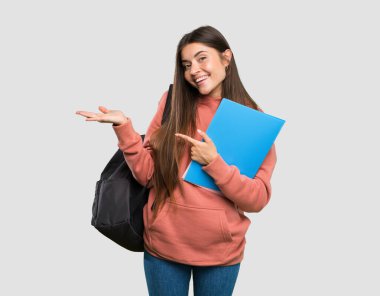 İzole gri arka plan üzerine bir reklam eklemek için avuç içinde taklit alanı hayali tutan deftertutan genç öğrenci kadın