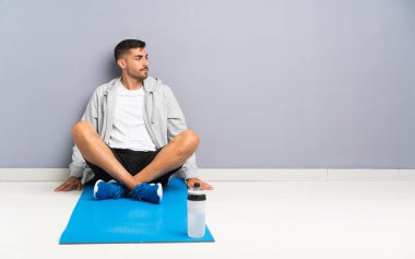 Spor adamı yerde oturuyor, yan bakıyor.