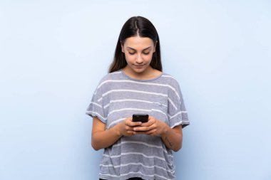 Cep telefonu kullanarak izole mavi arka plan üzerinde genç esmer kadın