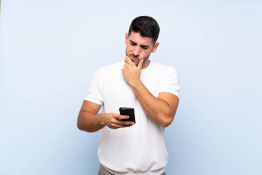 Kafkasyalı yakışıklı adam mavi arka plan üzerinde düşünüp bir mesaj gönderiyor.