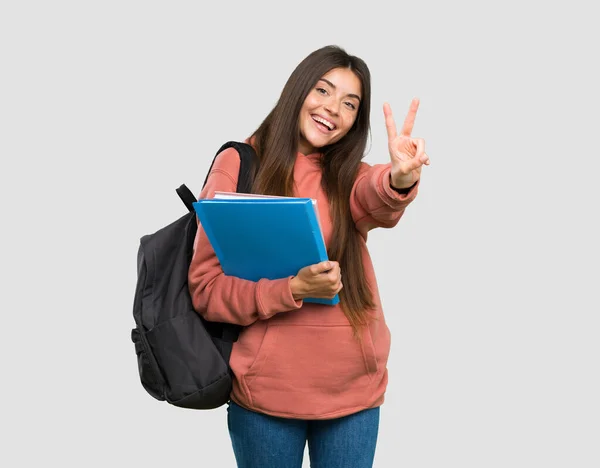 Giovane Studentessa Possesso Quaderni Sorridente Mostrando Segno Vittoria Sfondo Grigio — Foto Stock