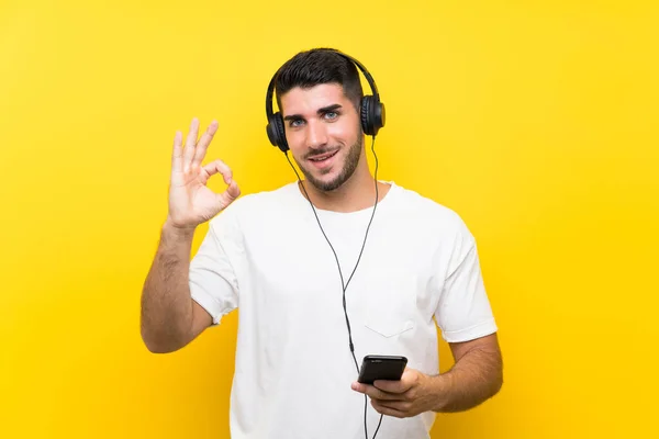 Молодой Красивый Мужчина Слушает Музыку Мобильного Над Изолированной Желтой Стеной — стоковое фото