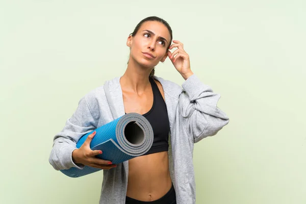 Giovane Donna Sportiva Con Stuoia Sfondo Verde Isolato Avendo Dubbi — Foto Stock