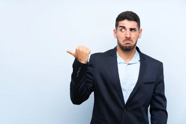 Hombre Guapo Sobre Fondo Azul Aislado Infeliz Apuntando Hacia Lado —  Fotos de Stock