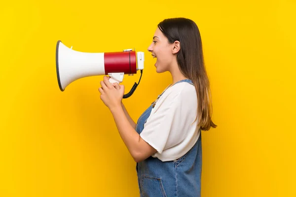 Jovem Mulher Dungarees Sobre Isolado Amarelo Fundo Gritando Através Megafone — Fotografia de Stock