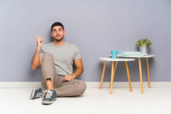 Jovem Homem Bonito Sentado Chão Apontando Com Dedo Indicador Uma — Fotografia de Stock