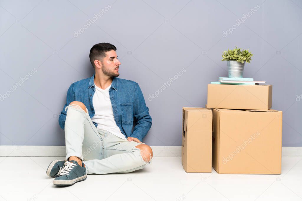 Handsome young man moving in new home among boxes looking side
