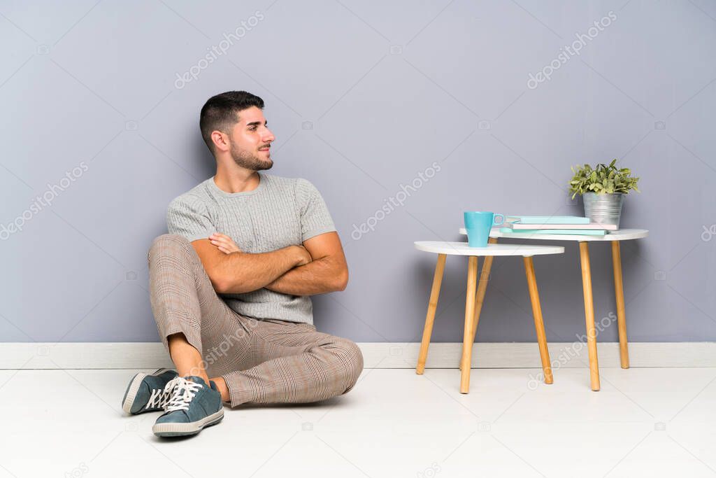 Young handsome man sitting on the floor looking to the side