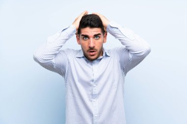 Kafkasyalı yakışıklı, yalıtılmış mavi arka planda, şaşırmış bir yüz ifadesi var.