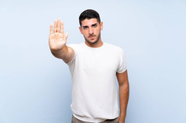 İzole edilmiş mavi arka planda beyaz yakışıklı adam dur hareketi yapıyor.