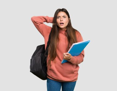 Elinde defterler tutan genç bir öğrenci kız hayal kırıklığına uğramış ve el ele tutuşmuş bir şekilde izole edilmiş gri arka planda duruyor.