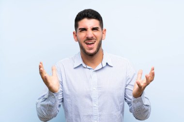 Kafkasyalı yakışıklı bir adam soyutlanmış mavi arka planda mutsuz ve hayal kırıklığına uğramış.