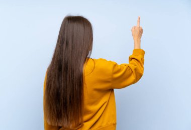 Kafkasyalı genç bir kadın, izole edilmiş mavi duvarın arkasında işaret parmağıyla işaret ediyor.