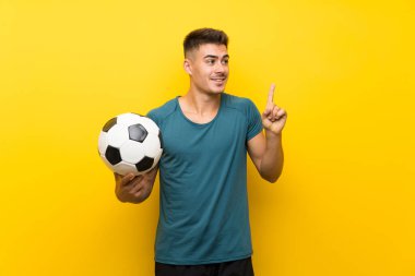 Yakışıklı genç futbolcu izole edilmiş sarı arka planda parmağını kaldırarak çözümü bulmaya çalışıyor.