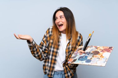 İzole edilmiş mavi arka planı olan genç ressam kadın. Şaşırtıcı yüz ifadesi var.