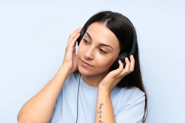 Jovem mulher ouvindo música sobre fundo azul isolado — Fotografia de Stock