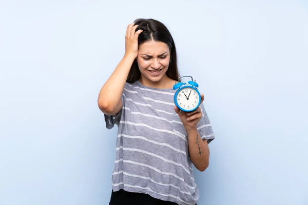 年轻的黑发女人在孤立的蓝色背景持有老式闹钟 — 图库照片