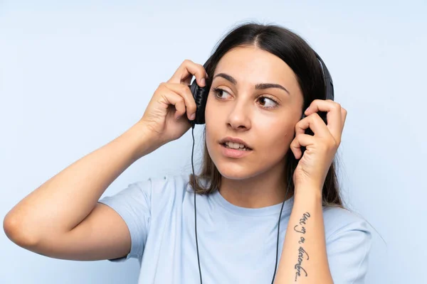 Mladá žena naslouchající hudbě přes izolované modré pozadí — Stock fotografie