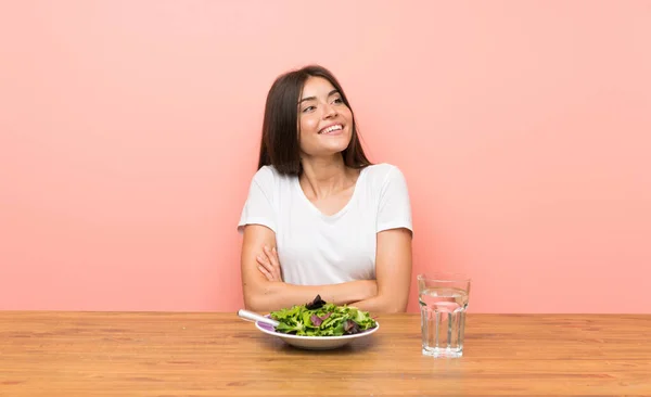 Young woman with a salad looking up while smiling