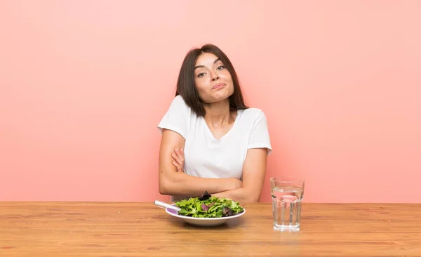 Young woman with a salad making doubts gesture while lifting the shoulders