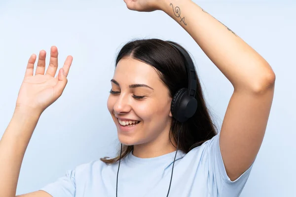 Mladá žena naslouchající hudbě přes izolované modré pozadí — Stock fotografie
