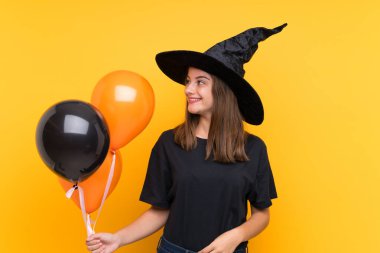 Cadılar bayramı partileri için elinde siyah ve turuncu balonlar tutan genç cadı.