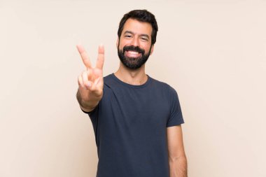 Sakallı adam gülümsüyor ve zafer işareti gösteriyor.