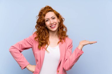 Bir reklam eklemek için avuç üzerinde copyspace hayali tutan izole mavi duvar üzerinde takım elbiseli Redhead kadın