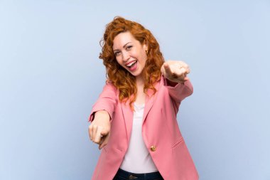 İzole edilmiş mavi duvar üzerindeki kızıl saçlı kadın gülümserken seni işaret ediyor.