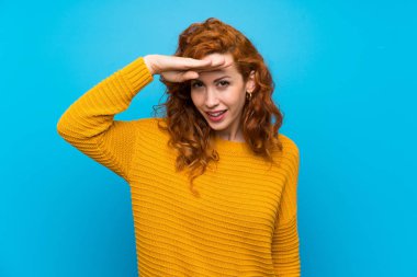 Kızıl saçlı, sarı kazaklı bir kadın, bir şeye bakmak için uzaklara bakıyor.