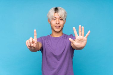 Asyalı genç adam izole edilmiş mavi arka planda altı parmaklı sayıyor.