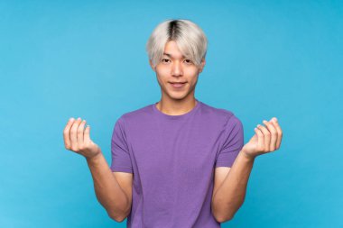 Asyalı genç adam soyutlanmış mavi arka planda para hareketi yapıyor.