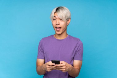 Asyalı genç adam izole edilmiş mavi arka plan şaşırdı ve bir mesaj gönderiyor.