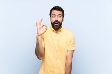 Mavi arka planda sakallı genç adam şaşırdı ve iyi olduğunu gösteriyor.