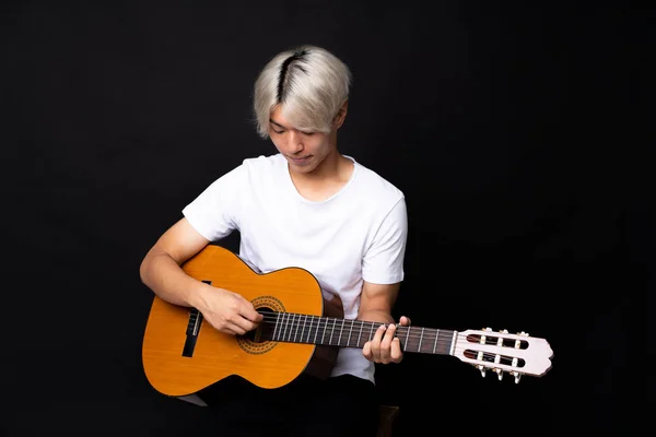 Mladý asijský muž s kytarou přes černé pozadí — Stock fotografie