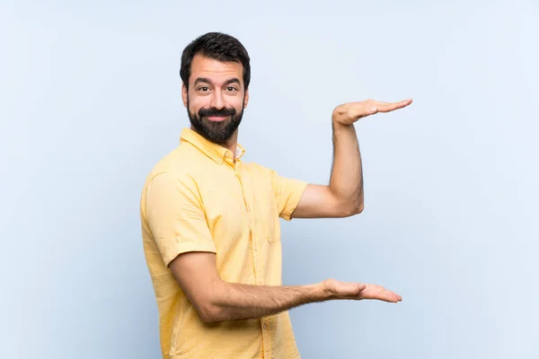 Joven Con Barba Sobre Fondo Azul Aislado Sosteniendo Espacio Para —  Fotos de Stock