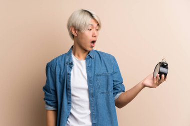 Asyalı genç bir adam izole edilmiş arka planda klasik çalar saat tutuyor.