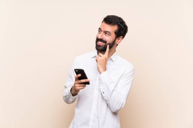 Sakallı genç adam cep telefonu tutuyor. Kafasını kaldırırken bir fikir düşünüyor.