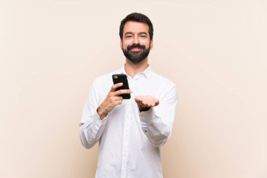 Elinde cep telefonu olan sakallı genç bir adam bir ilan vermek için avucunun içinde hayali bir şey tutuyor.