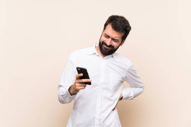 Sırt ağrısı çeken sakallı genç bir adam çabaladığı için cep telefonu tutuyor.