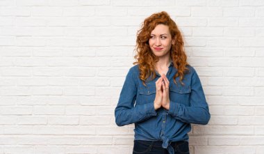 Kızıl saçlı kadın beyaz tuğla duvarın üstünde bir şeyler çeviriyor.