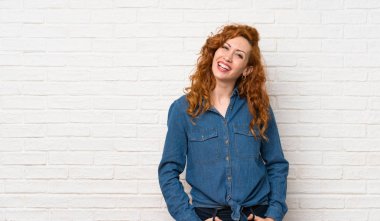 Beyaz tuğla duvarın üzerinde gülümseyen kızıl saçlı kadın.