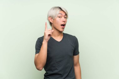 Asyalı genç adam yeşil arka planda, parmağını kaldırarak çözümü bulmaya çalışıyor.