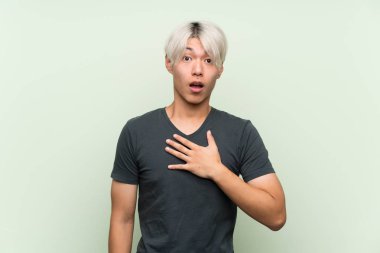 Asyalı genç adam yeşil arka planda kaldı. Şaşırdı ve şaşırdı.