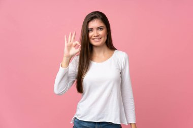 İzole edilmiş pembe arka planda genç bir kadın parmaklarıyla işaret veriyor.